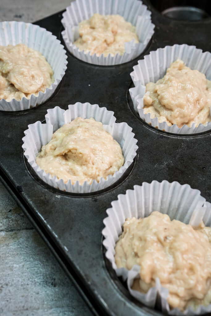Placing scoops of muffin batter into a muffin pan with paper liners