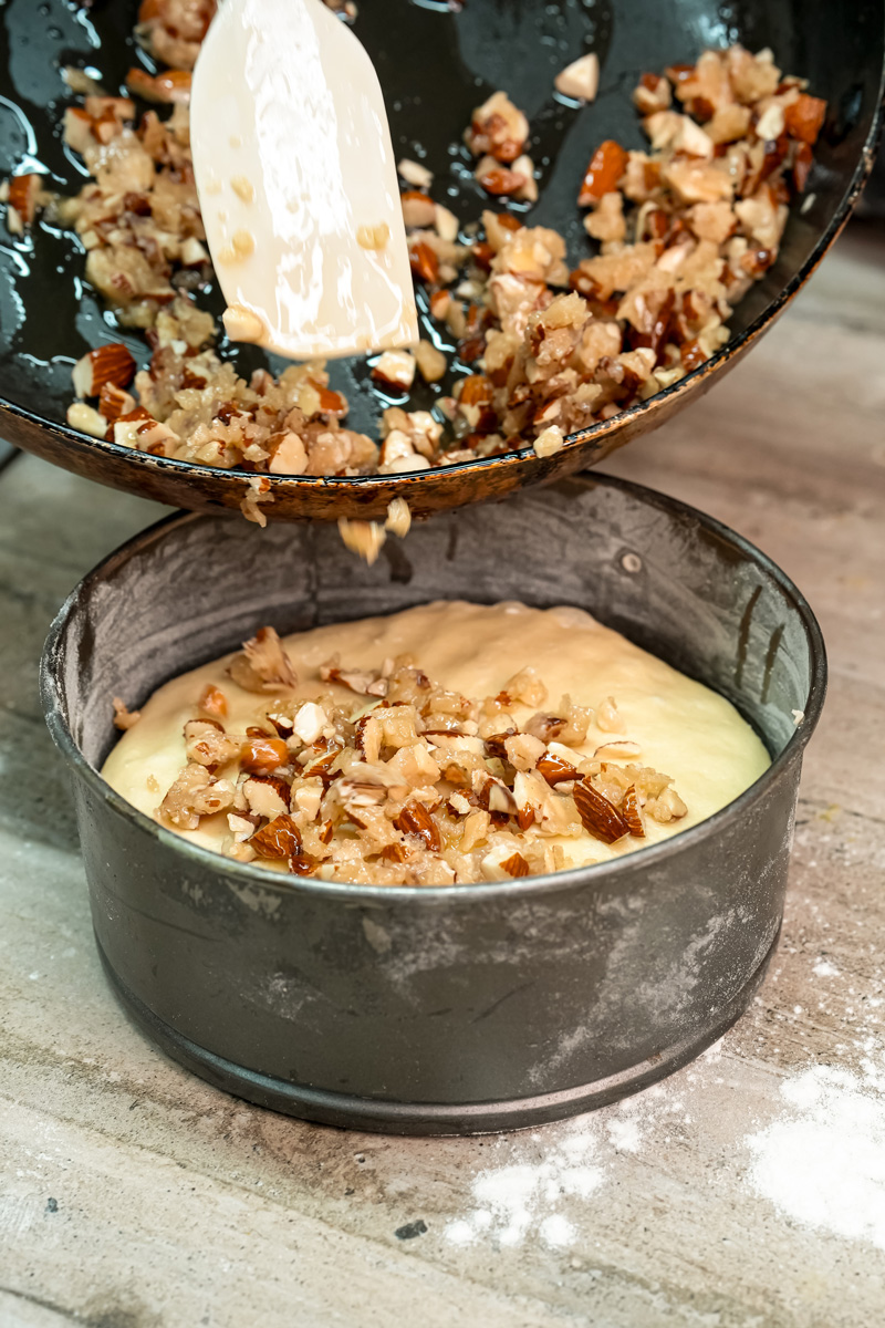 Pouring honey almond topping over cake batter in baking pan