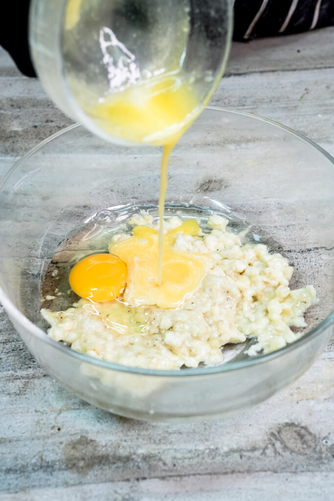 Pouring melted butter or oil into a glass bowl with mashed bananas and eggs for muffins