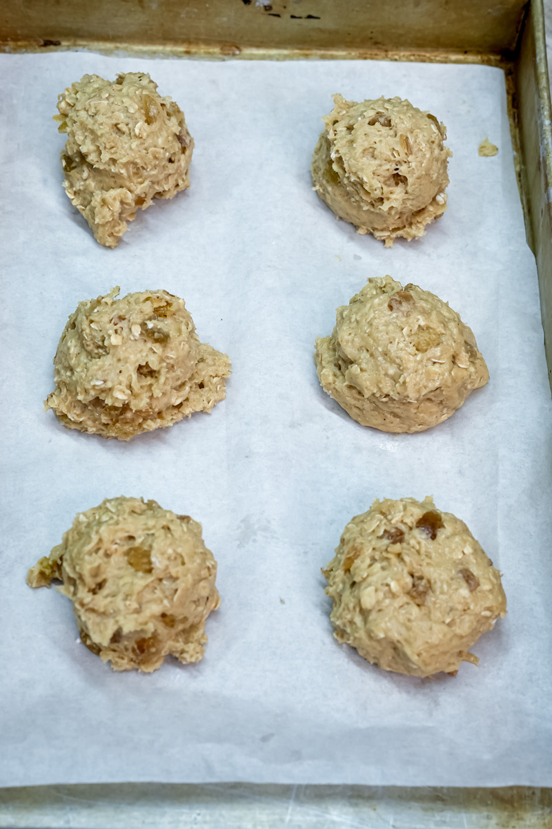 Raw oatmeal raisin cookie dough portions on parchment-lined baking sheet