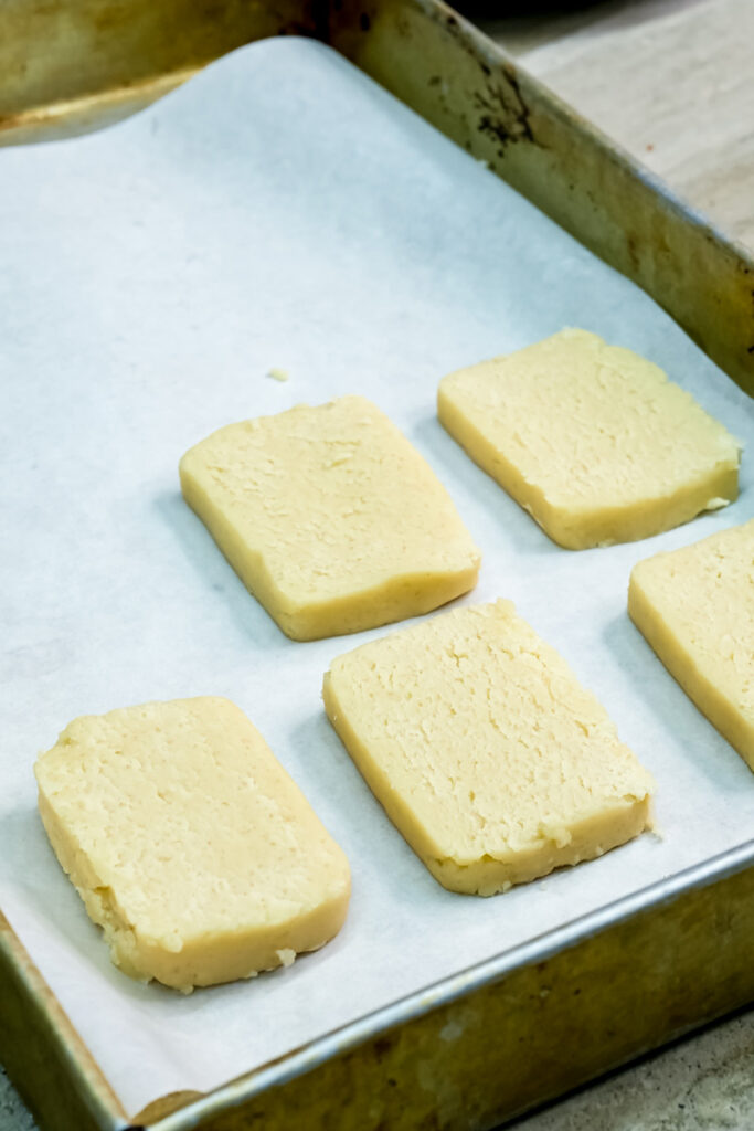 Raw shortbread cookie rectangles arranged on parchment-lined baking sheet