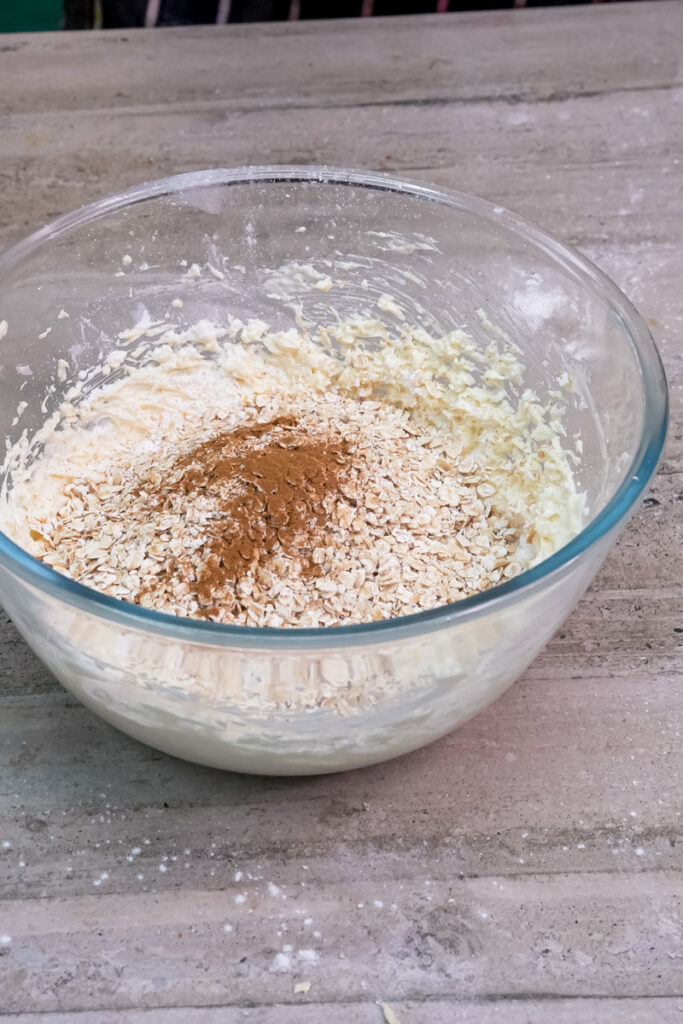 Rolled oats and ground cinnamon are added to the cookie dough mixture