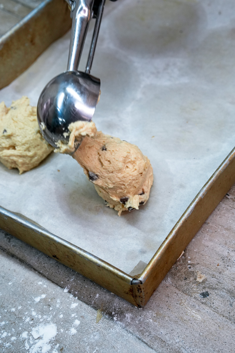 Scooping cookie dough onto a baking sheet lined with parchment paper