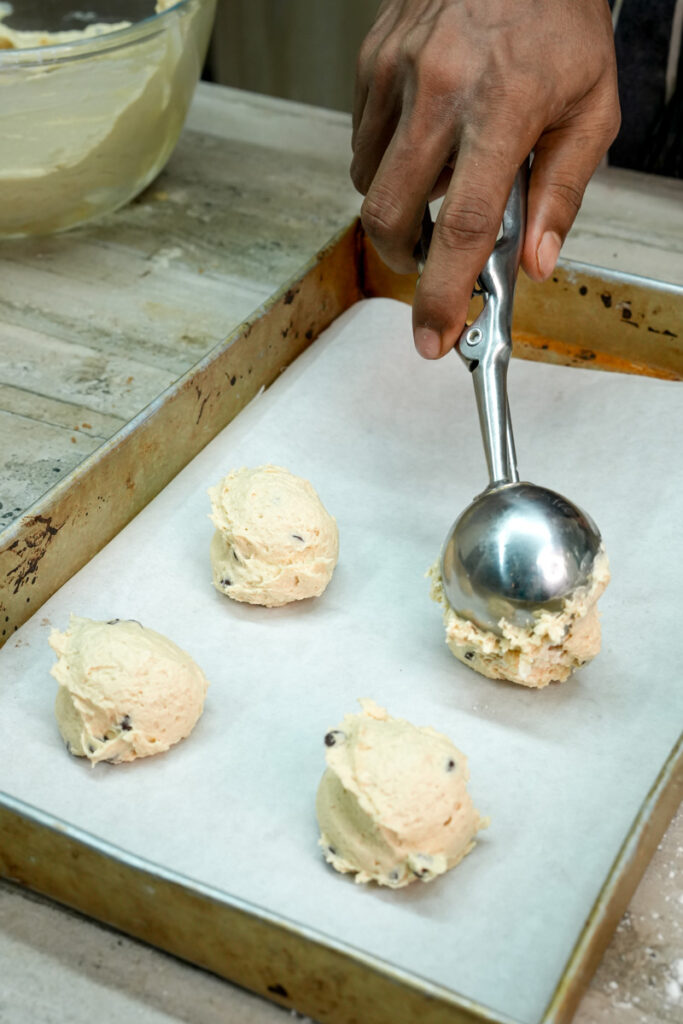 Scooping portions of cookie dough onto a parchment-lined baking sheet
