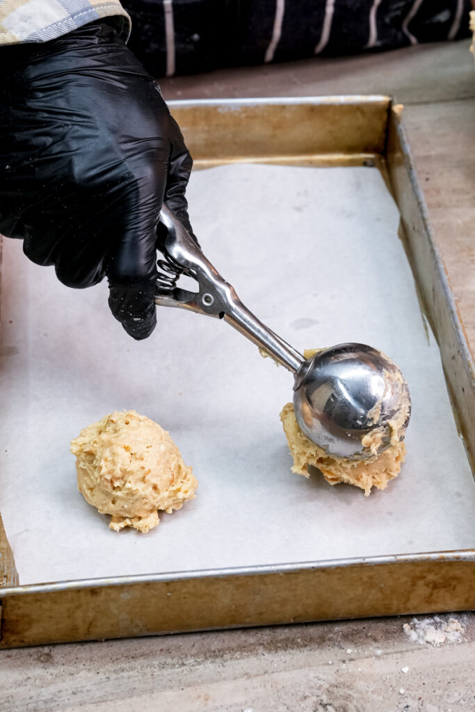 Scooping ranger cookie dough onto parchment-lined baking sheet
