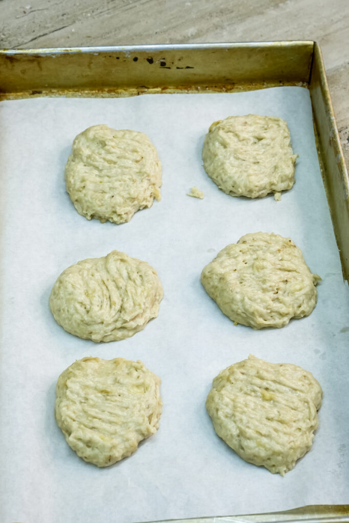 Several scoops of banana cookie dough, flattened with a fork, arranged on a parchment-lined baking sheet
