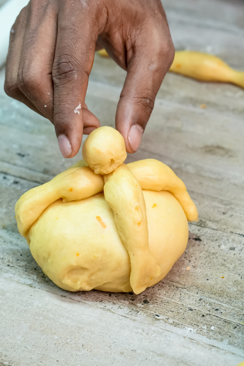 Shaping pan de muerto dough into traditional flower pattern