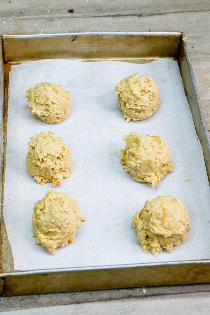 Six portions of ranger cookie dough on parchment paper before baking