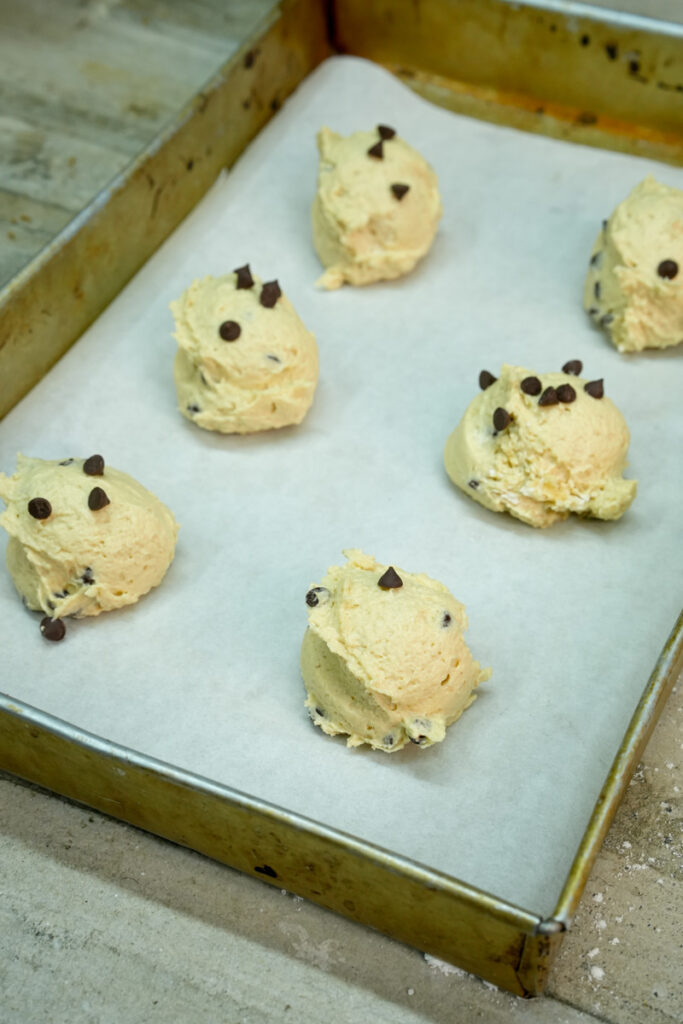 Six scoops of cookie dough with chocolate chips on a baking sheet