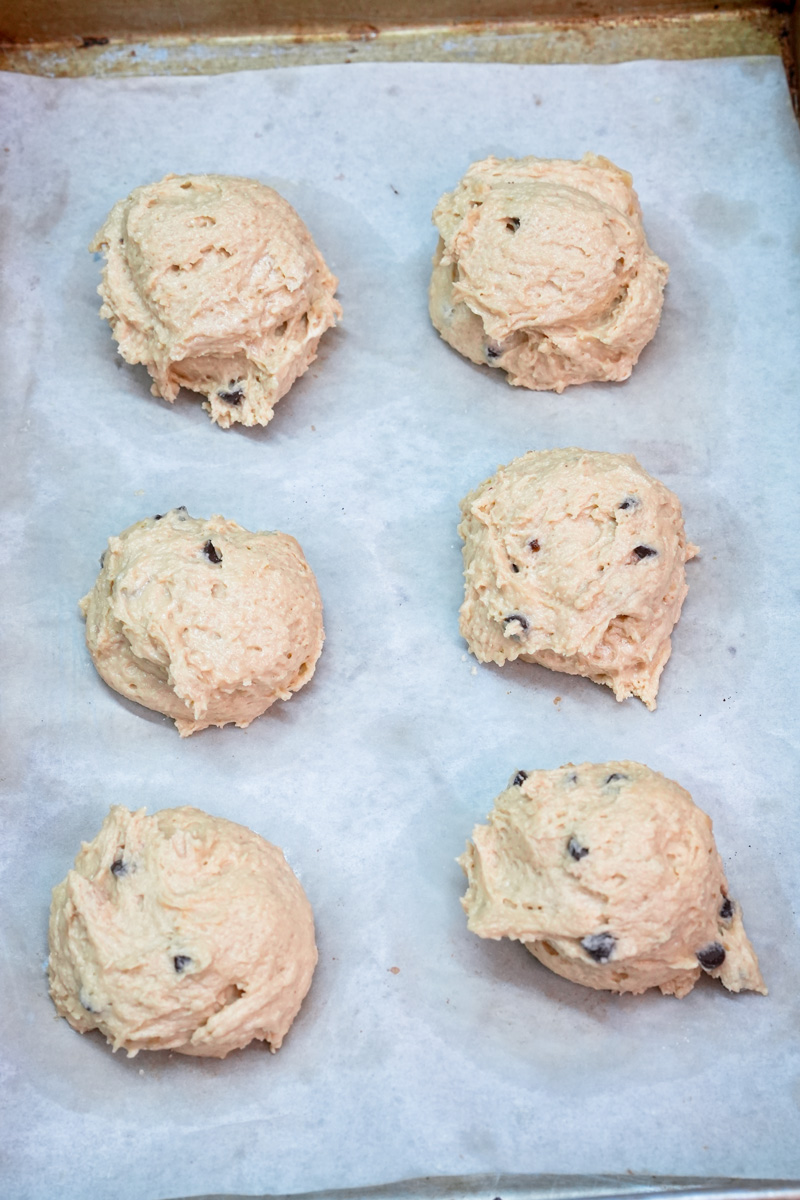 Six scoops of raw chocolate chip cookie dough on a baking sheet