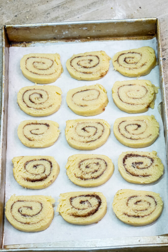 Sliced cinnamon roll cookies arranged on a baking sheet lined with parchment paper