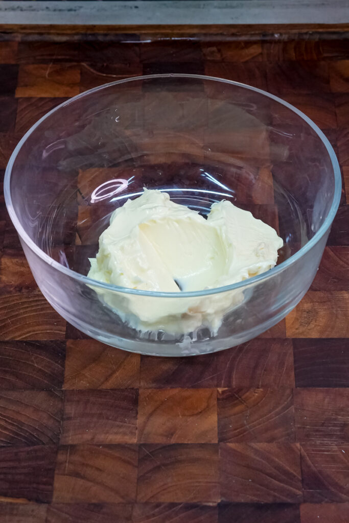 Softened butter in a clear bowl on a wooden cutting board