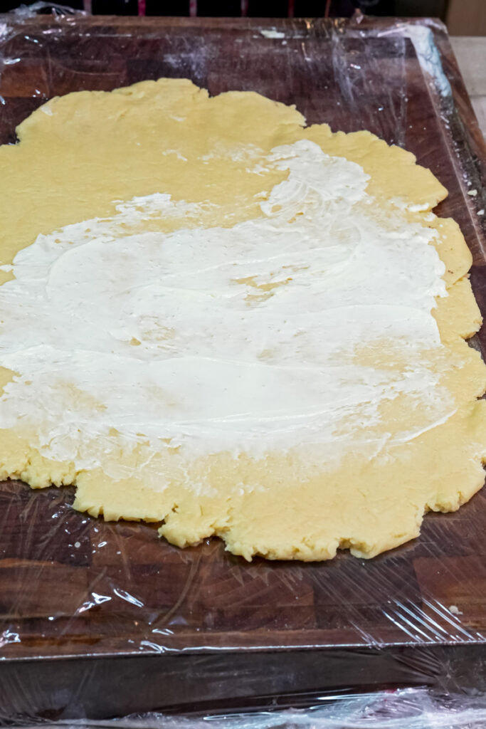 Spreading a layer of cream cheese frosting over the rolled-out cookie dough