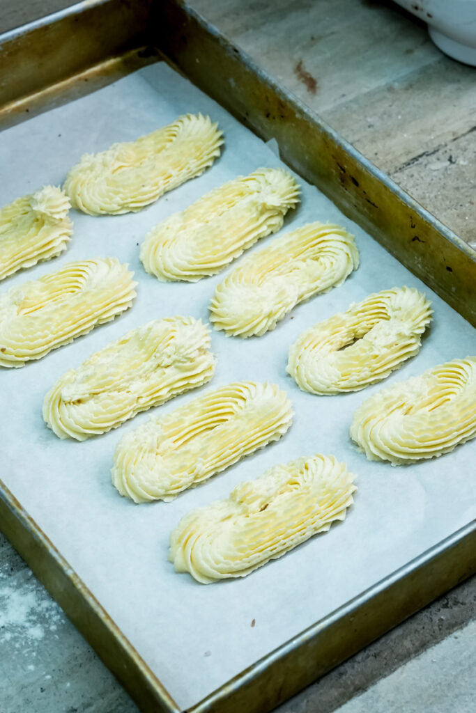 Spritz cookie dough piped into various shapes on a baking sheet lined with parchment paper