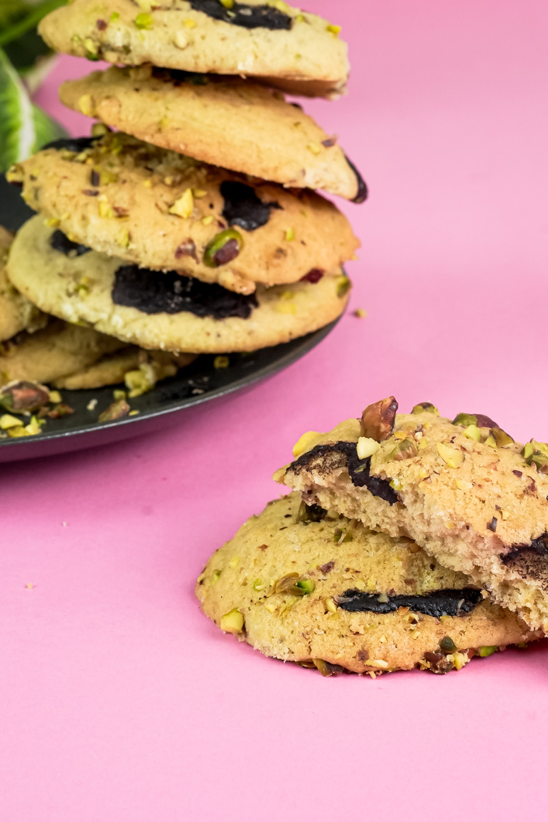 Stack of pistachio cookies next to a broken cookie on a pink surface