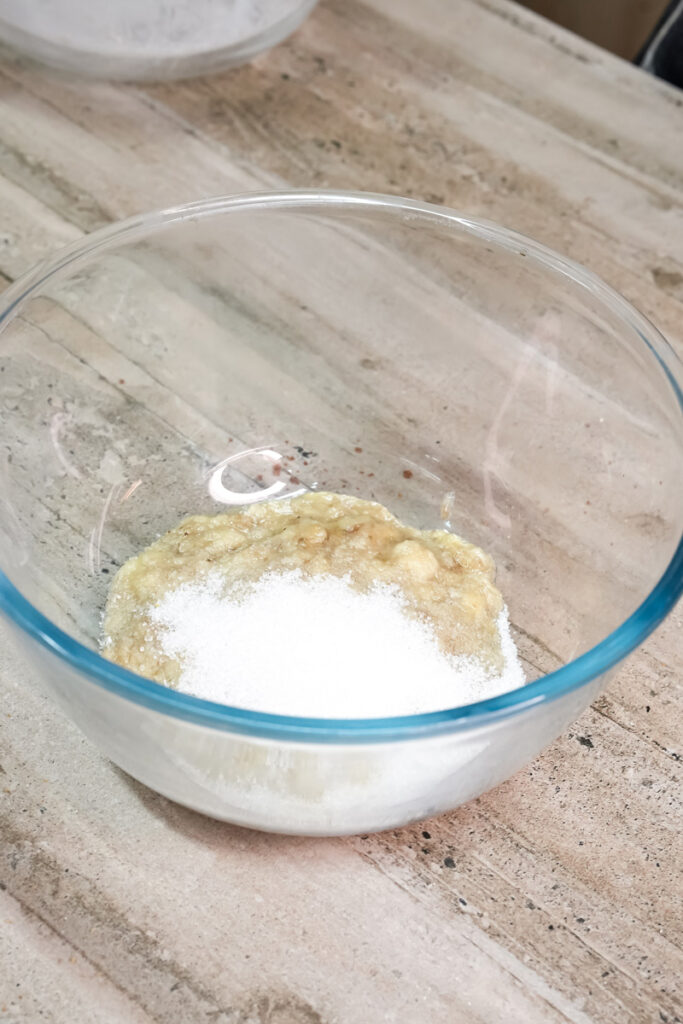 Sugar being added to the mashed bananas in a bowl