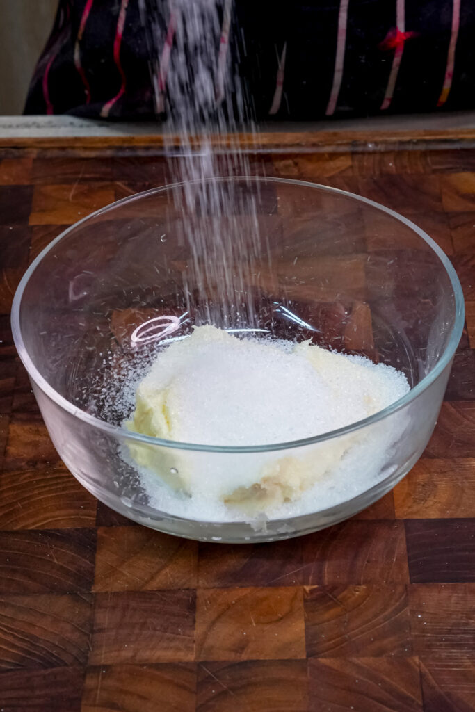 Sugar being poured onto the softened butter in a bowl
