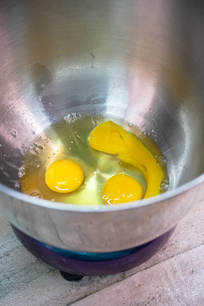 Three eggs cracked in a silver mixing bowl for a cake recipe