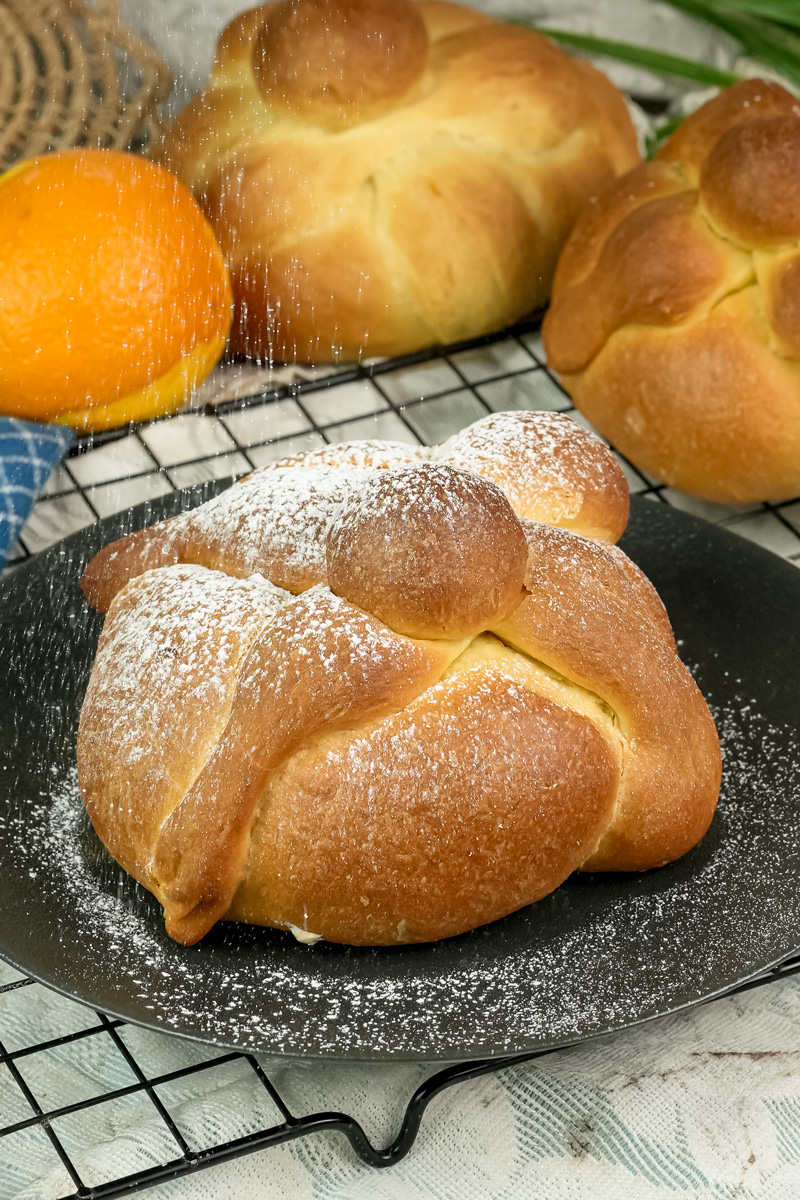 Traditional Pan de Muerto bread with decorative bone shapes dusted with powdered sugar on cooling rack