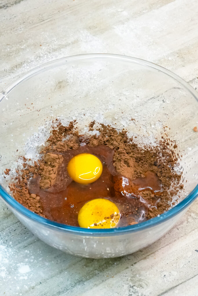 Two eggs and cocoa powder mixed in a clear glass bowl