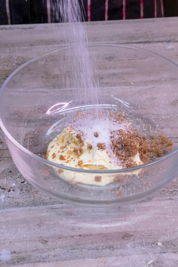 White sugar being poured into the bowl with butter and brown sugar