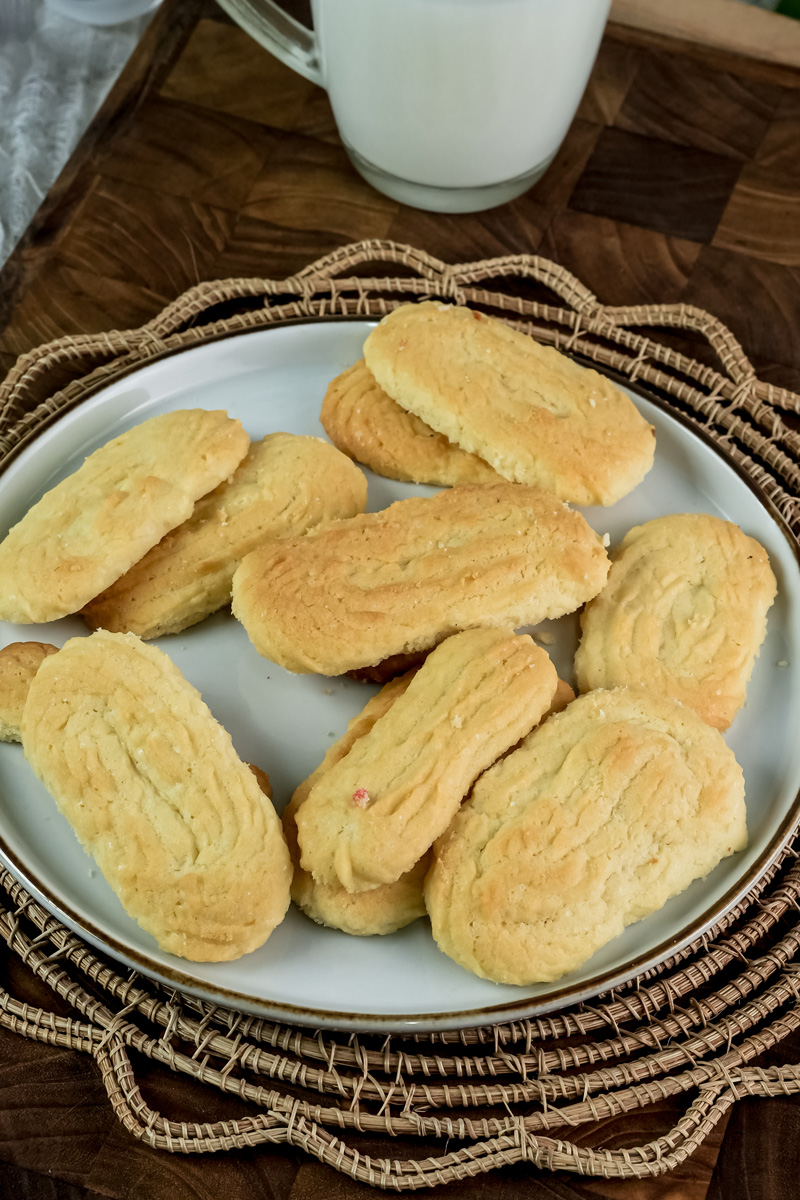 A plate of baked spritz cookies next to a glass of milk, shot from above