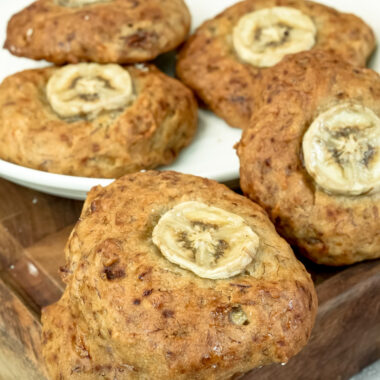 A single banana cookie with a sliced banana on top, in focus, with other cookies blurred in the background