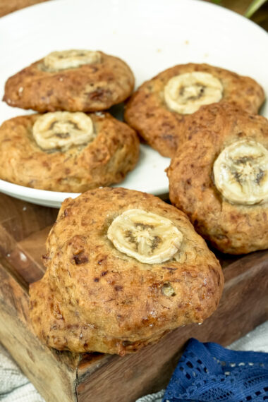 A single banana cookie with a sliced banana on top, in focus, with other cookies blurred in the background