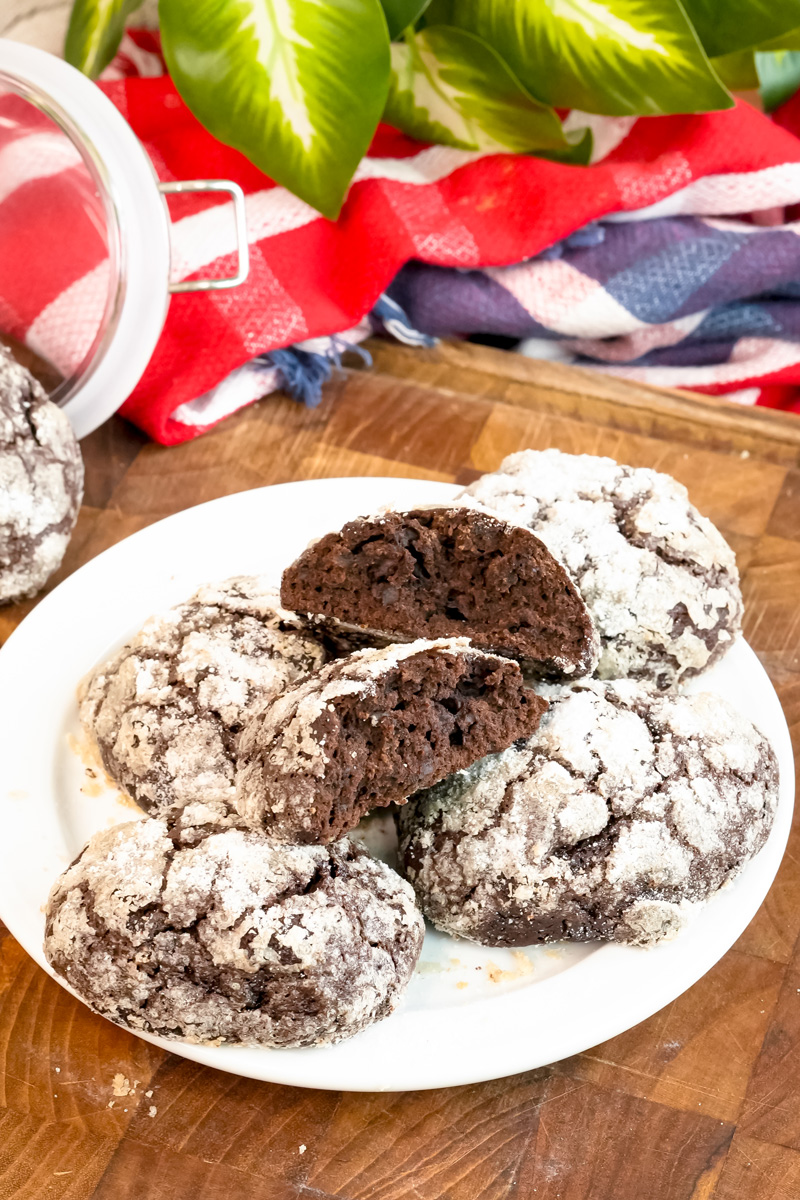 A close-up of a broken chocolate crinkle cookie on a plate with others.