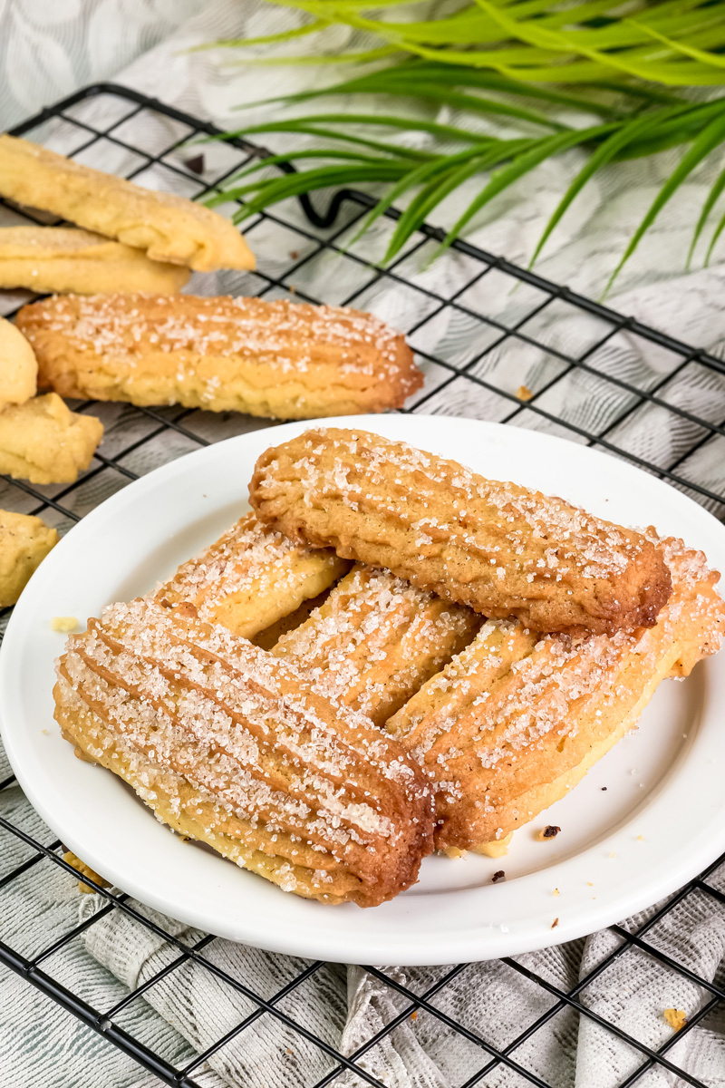 A beautiful, overhead shot of a white plate piled with churro cookies, sprinkled with sugar