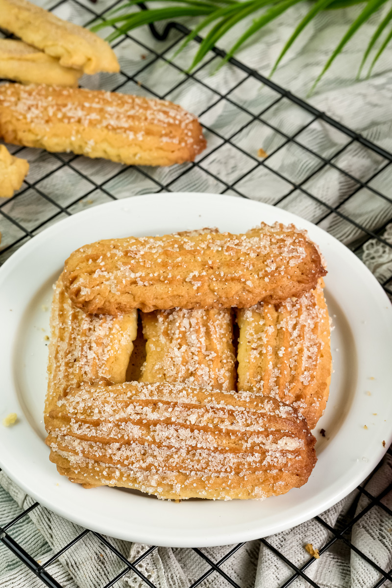 A plate of crispy churro cookies with cinnamon sugar, with more cookies in the background on a wire rack