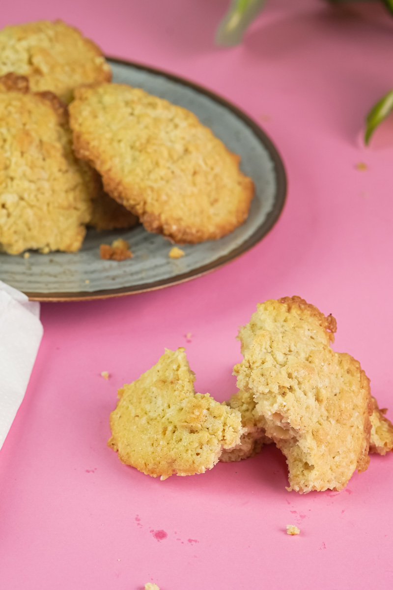 A delicious broken oatmeal cookie on a pink background, with more cookies visible on a plate in the background