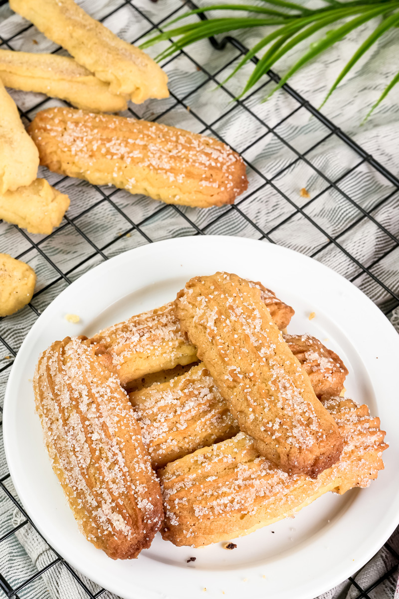 Stack of delicious churro cookies on a white plate with more cookies in the background
