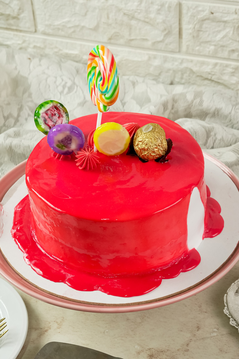A finished drip cake on a cake stand with candy decorations