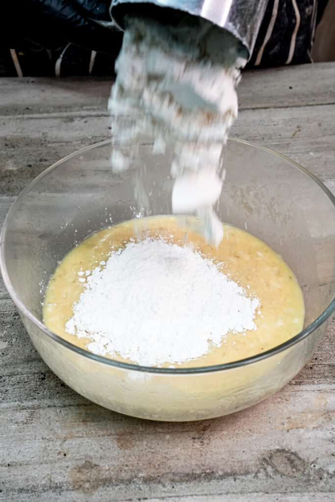 Sifting dry flour mixture into the wet ingredients for banana protein muffin batter