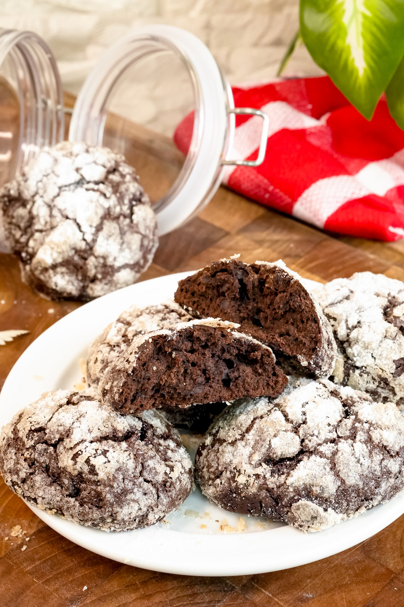 A plate of fresh chocolate crinkle cookies, with one split open to reveal the moist, brownie-like center.