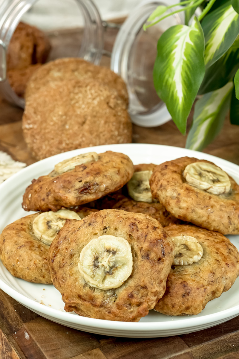 A plate of freshly baked banana cookies with a green plant in the background, adding a touch of nature