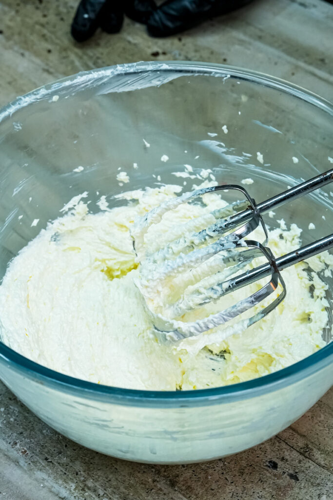 A close-up of a glass bowl with smooth, fluffy creamed butter and sugar being mixed by a hand mixer