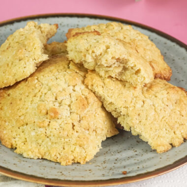 A close-up of golden brown oatmeal cookies on a grey plate, with a half-eaten cookie in the foreground