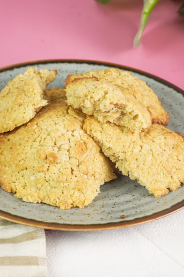 A close-up of golden brown oatmeal cookies on a grey plate, with a half-eaten cookie in the foreground