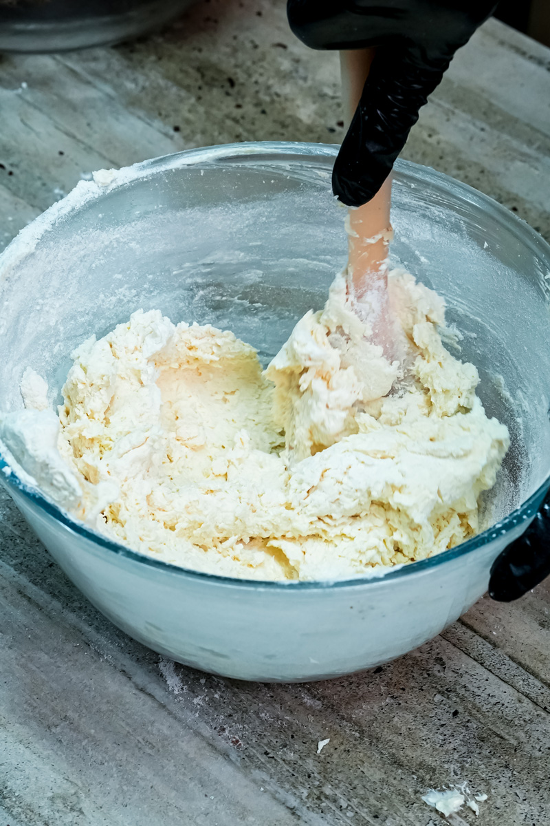A hand mixing spritz cookie dough in a bowl, showing the flour being incorporated into the wet ingredients