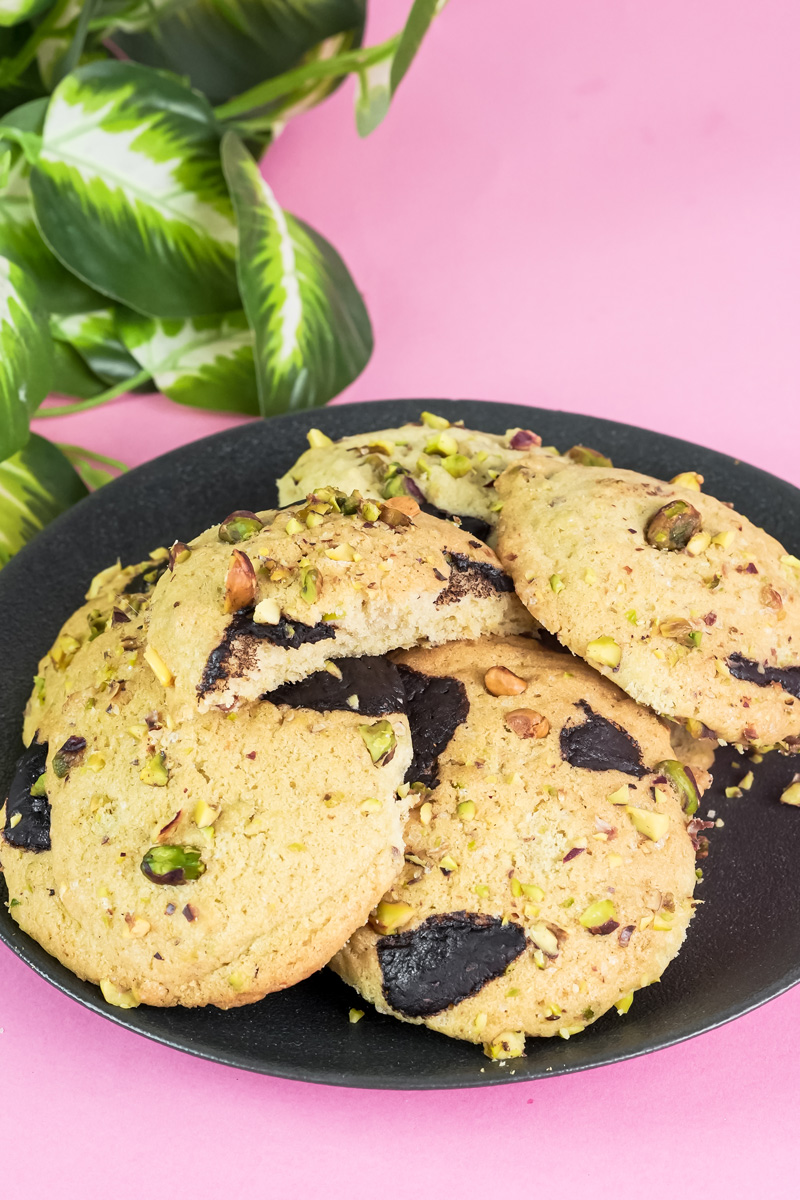 A plate of homemade pistachio cookies with chocolate chunks on a pink background