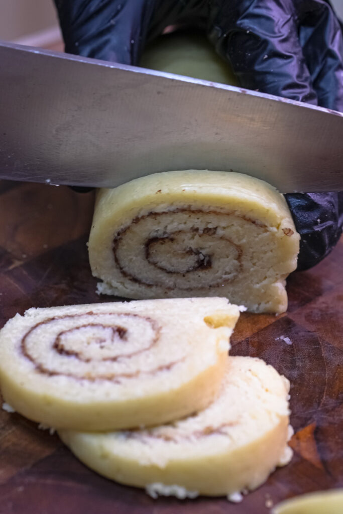 Close-up of a knife slicing cookie dough, showing the detailed cinnamon swirl
