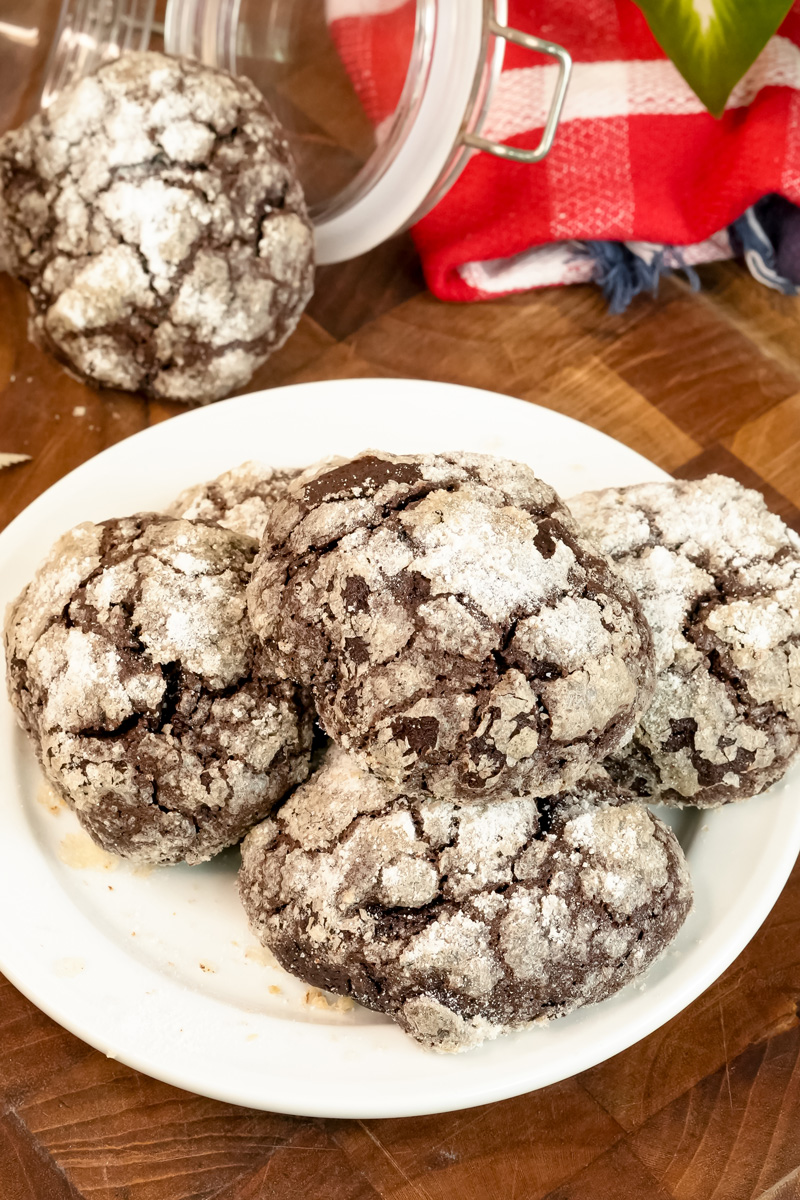 A close-up shot of a stack of freshly baked chocolate crinkle cookies, with a glass jar in the background.