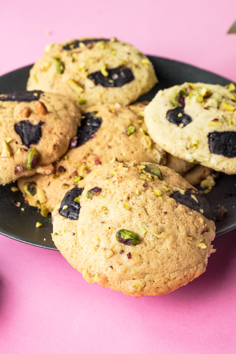A pile of pistachio cookies on a black plate, showcasing the chocolate and nuts