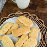 An overhead view of a plate of baked spritz cookies and a glass of milk on a wooden board