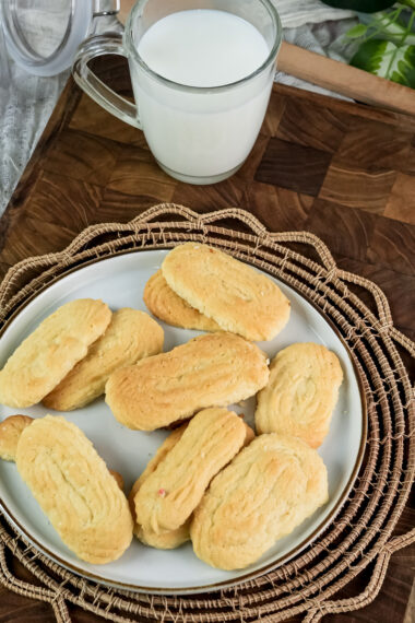 An overhead view of a plate of baked spritz cookies and a glass of milk on a wooden board