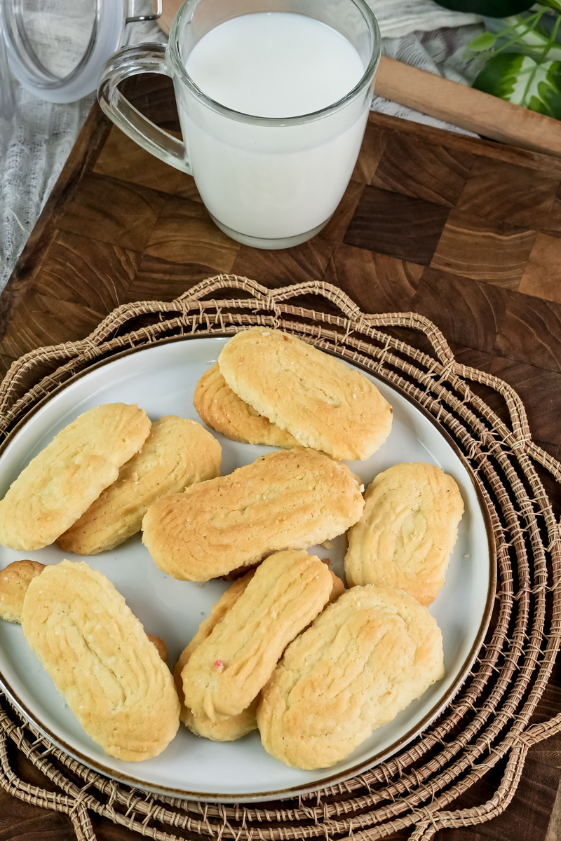 An overhead view of a plate of baked spritz cookies and a glass of milk on a wooden board