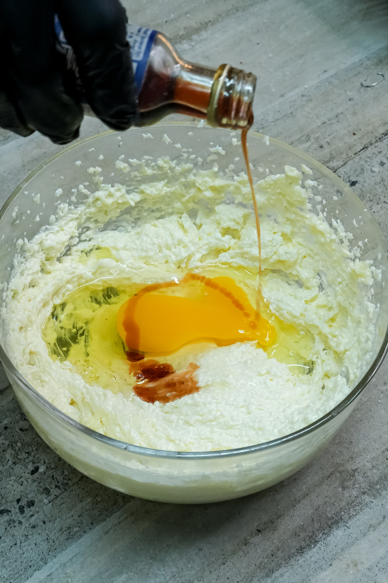 A hand pouring vanilla extract and cracking an egg into the creamed butter and sugar