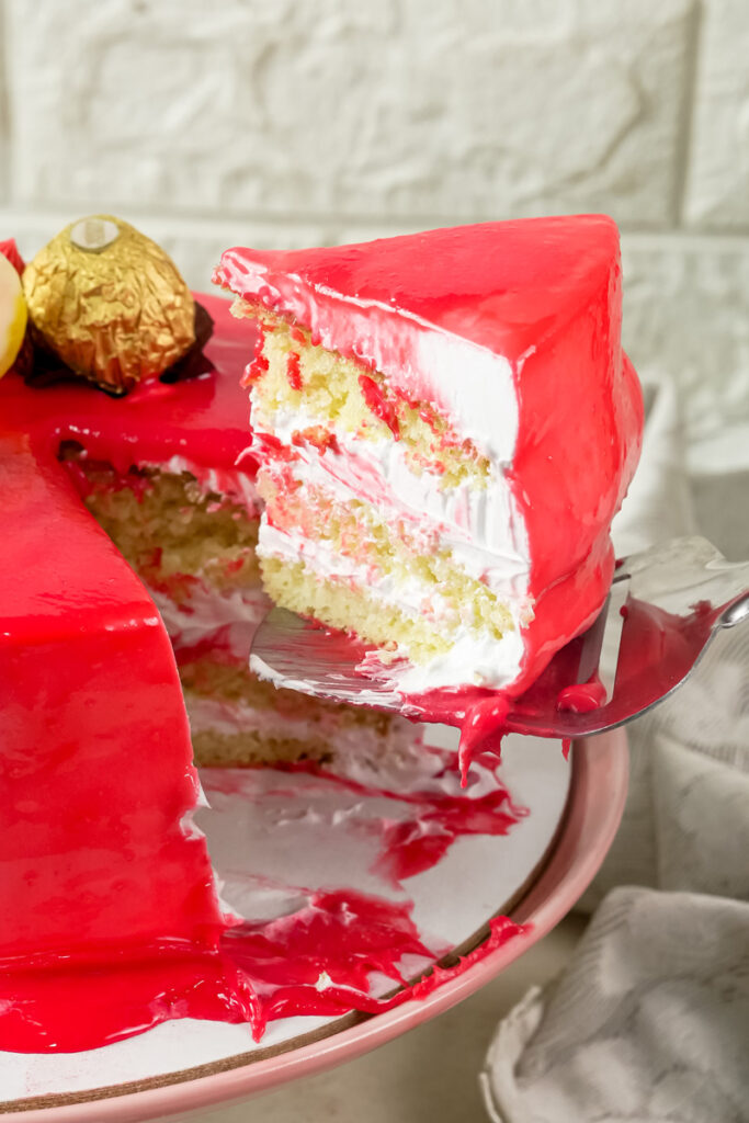 A slice of red drip cake with a spoon, showing the layers of sponge and frosting